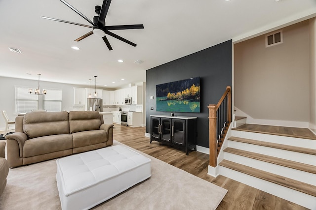 living room with ceiling fan with notable chandelier and light hardwood / wood-style floors