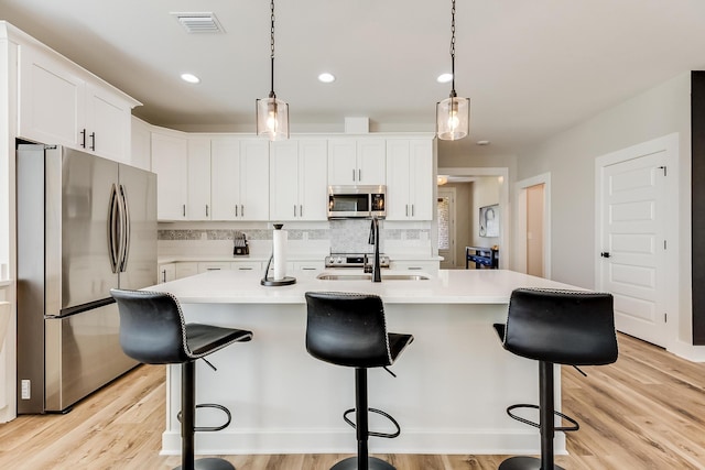 kitchen featuring a kitchen island with sink, white cabinetry, stainless steel appliances, and decorative light fixtures