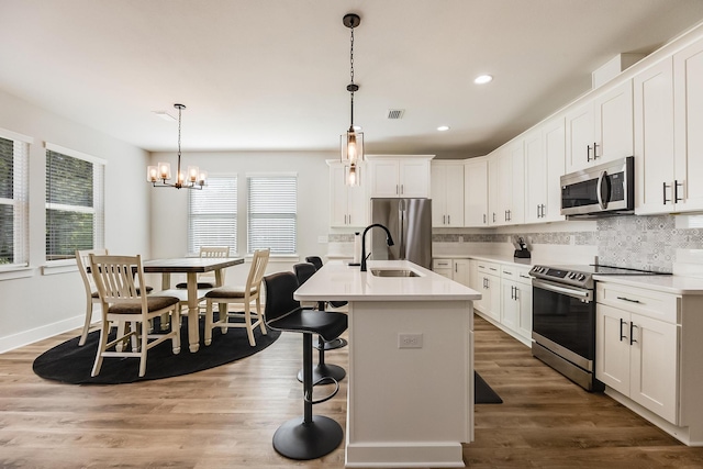 kitchen featuring white cabinetry, hanging light fixtures, a chandelier, a kitchen island with sink, and appliances with stainless steel finishes