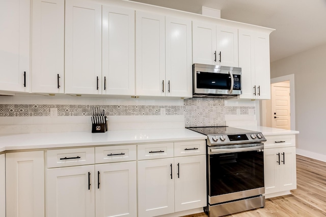 kitchen featuring tasteful backsplash, white cabinets, light hardwood / wood-style floors, and appliances with stainless steel finishes