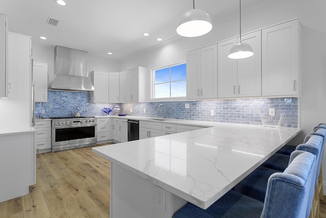 kitchen with white cabinetry, wall chimney range hood, high end stove, pendant lighting, and a breakfast bar