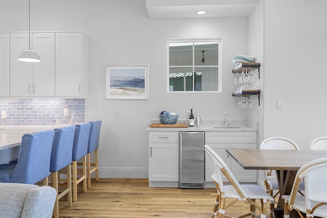 kitchen featuring pendant lighting, white cabinets, sink, light wood-type flooring, and tasteful backsplash