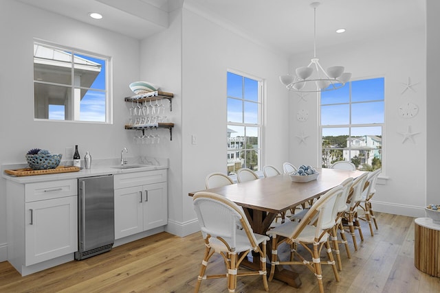 dining space featuring indoor wet bar, light hardwood / wood-style floors, an inviting chandelier, and ornamental molding