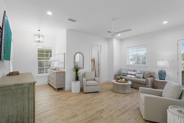 living room featuring ceiling fan with notable chandelier and light hardwood / wood-style flooring