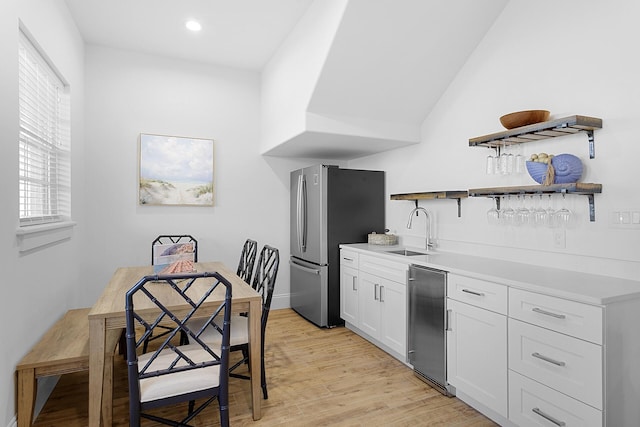 kitchen featuring stainless steel refrigerator, sink, light hardwood / wood-style flooring, white cabinetry, and lofted ceiling