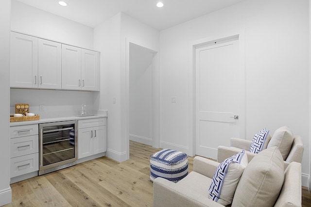 bar featuring sink, white cabinets, beverage cooler, and light hardwood / wood-style floors