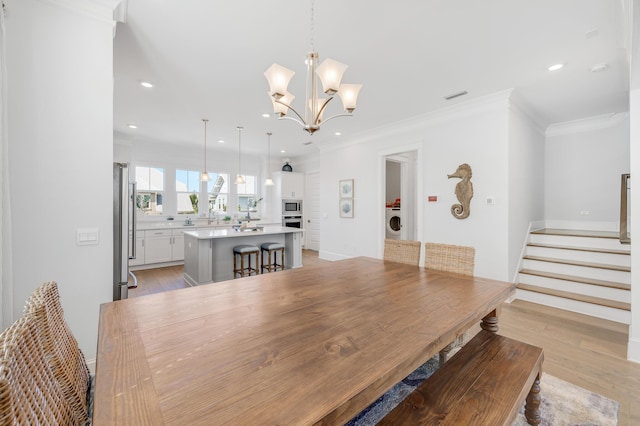 dining area featuring washer / clothes dryer, ornamental molding, a chandelier, and light hardwood / wood-style floors