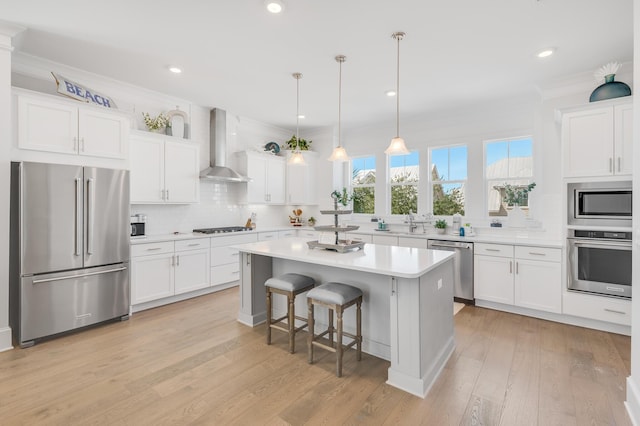 kitchen with white cabinets, wall chimney range hood, hanging light fixtures, appliances with stainless steel finishes, and a kitchen island