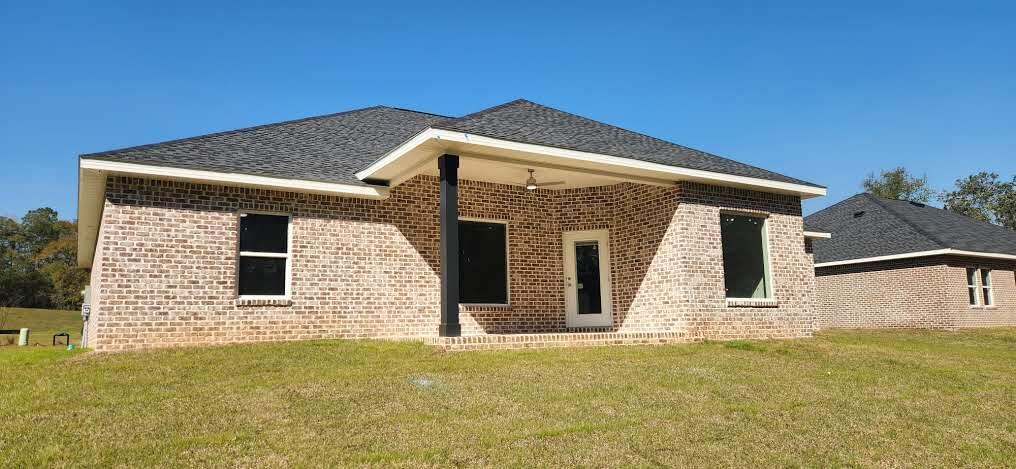 rear view of house with brick siding, a lawn, and roof with shingles