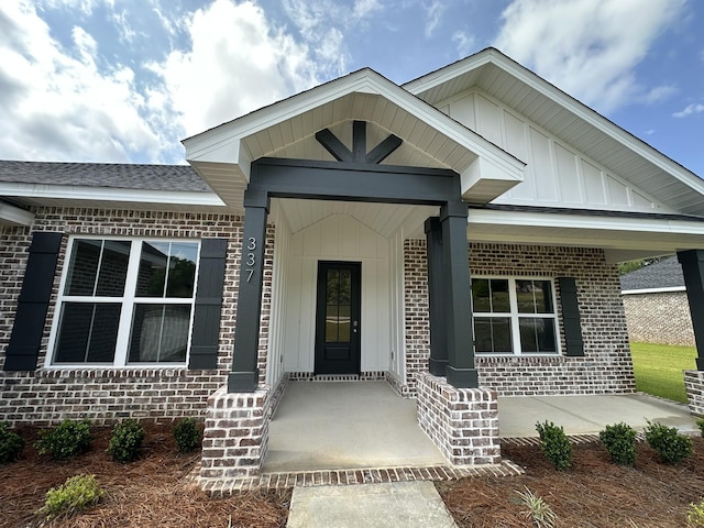 entrance to property featuring board and batten siding, a porch, a shingled roof, and brick siding