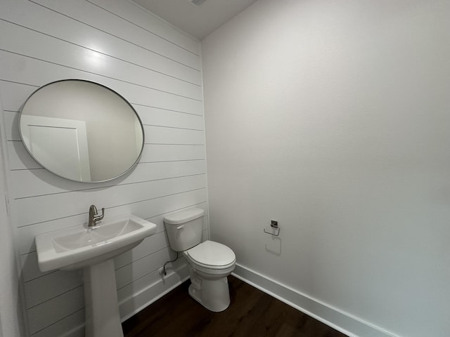 half bathroom with wood walls, wood finished floors, toilet, and baseboards