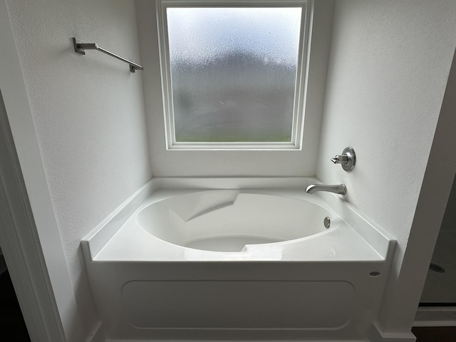 full bath with a garden tub, a textured wall, and a wealth of natural light