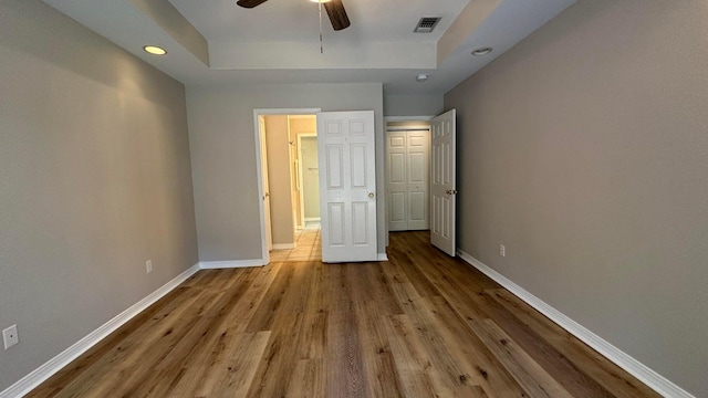 unfurnished bedroom featuring light wood-type flooring, ceiling fan, and a tray ceiling