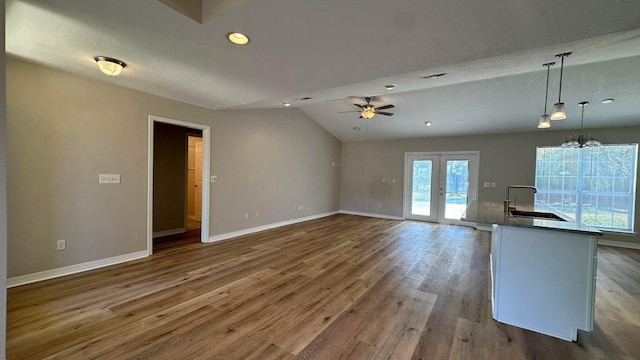 unfurnished living room featuring a textured ceiling, hardwood / wood-style flooring, sink, lofted ceiling, and ceiling fan with notable chandelier