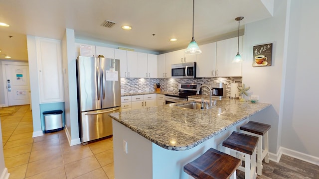 kitchen featuring white cabinetry, sink, kitchen peninsula, decorative light fixtures, and appliances with stainless steel finishes