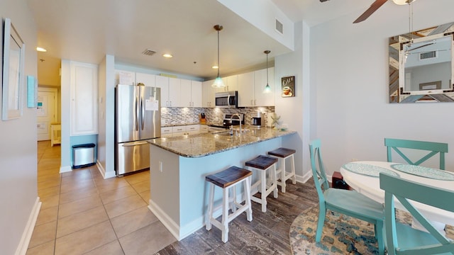 kitchen featuring kitchen peninsula, stainless steel appliances, decorative light fixtures, white cabinetry, and a breakfast bar area