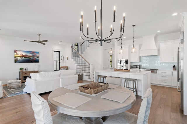 dining space with ceiling fan with notable chandelier and light wood-type flooring