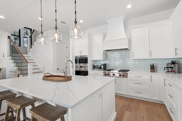 kitchen featuring a center island with sink, white cabinets, custom range hood, and stainless steel appliances