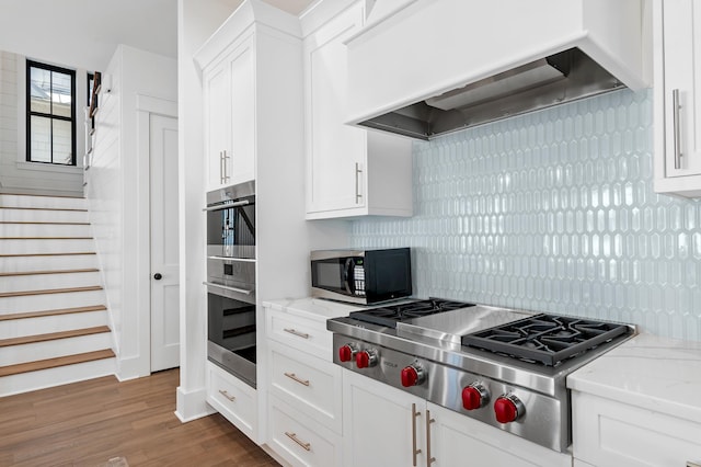 kitchen featuring decorative backsplash, light stone counters, custom exhaust hood, stainless steel appliances, and white cabinetry