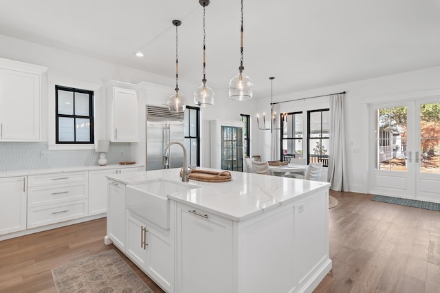 kitchen featuring a kitchen island with sink, french doors, built in refrigerator, light stone countertops, and white cabinetry