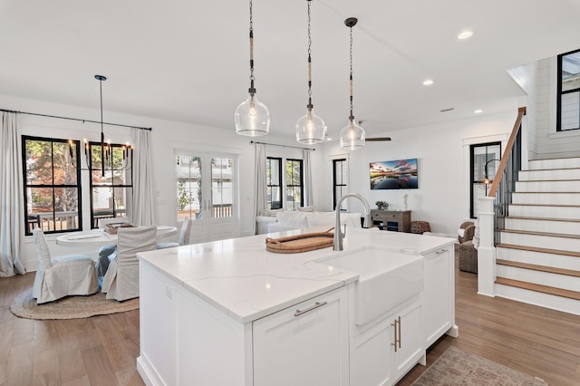 kitchen with a kitchen island with sink, sink, light stone countertops, decorative light fixtures, and white cabinetry