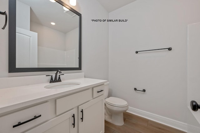 bathroom featuring toilet, baseboards, wood finished floors, and vanity