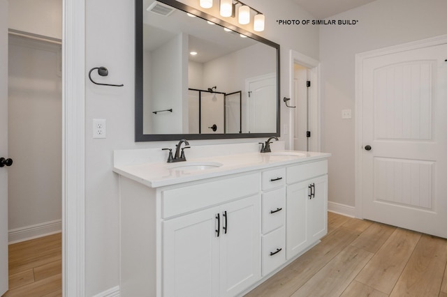 bathroom with baseboards, visible vents, a shower with door, wood finished floors, and a sink