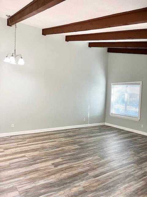 spare room with beamed ceiling, wood-type flooring, and a chandelier