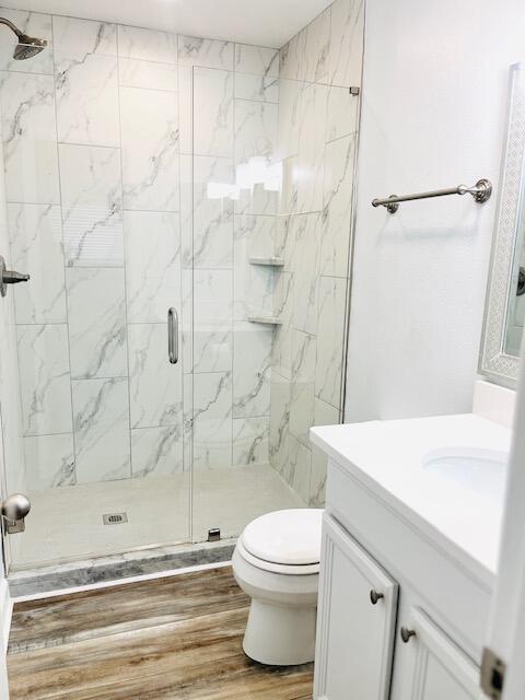 bathroom with hardwood / wood-style floors, vanity, toilet, and a shower with shower door