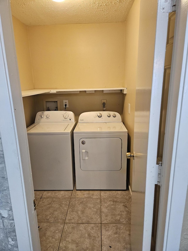 washroom featuring washer and clothes dryer, light tile patterned flooring, and a textured ceiling