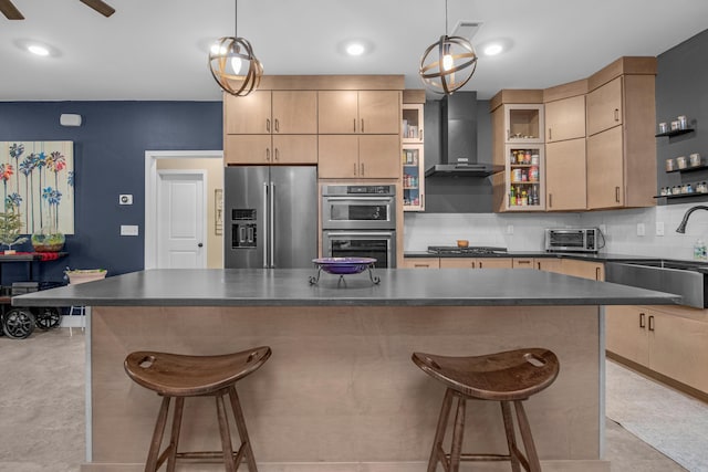 kitchen featuring wall chimney range hood, decorative backsplash, light brown cabinetry, appliances with stainless steel finishes, and decorative light fixtures