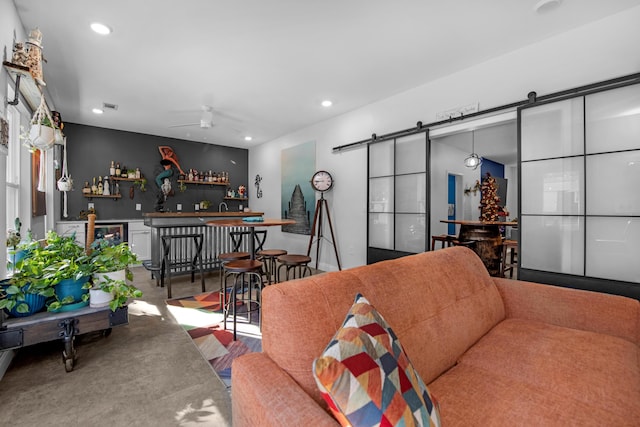 living room with ceiling fan, a barn door, and bar