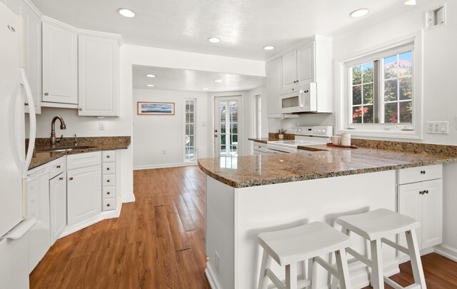 kitchen with white appliances, plenty of natural light, a sink, white cabinets, and light wood-type flooring