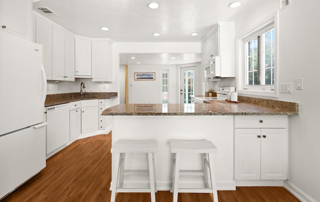 kitchen with visible vents, wood finished floors, white appliances, a peninsula, and white cabinets