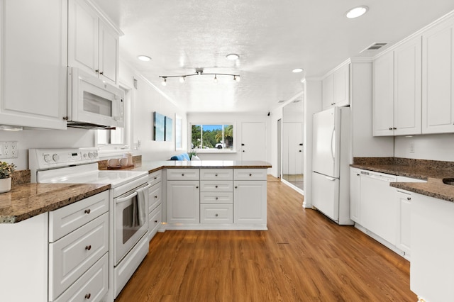 kitchen with white appliances, white cabinets, light hardwood / wood-style flooring, dark stone countertops, and kitchen peninsula