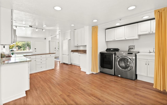 clothes washing area featuring washing machine and clothes dryer, light hardwood / wood-style flooring, cabinets, and sink