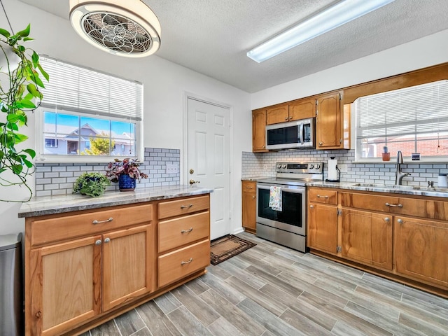 kitchen with sink, stainless steel appliances, light hardwood / wood-style flooring, a textured ceiling, and decorative backsplash