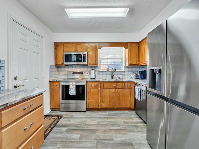 kitchen with backsplash, sink, a textured ceiling, light stone counters, and stainless steel appliances