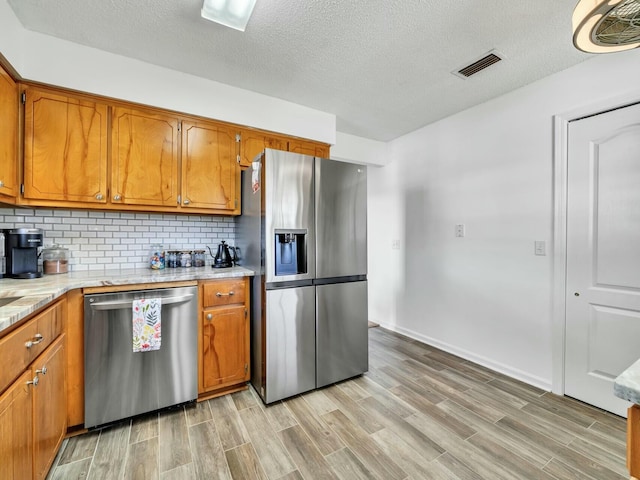 kitchen with decorative backsplash, appliances with stainless steel finishes, a textured ceiling, and light hardwood / wood-style floors