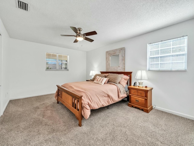 bedroom featuring ceiling fan, light colored carpet, and a textured ceiling