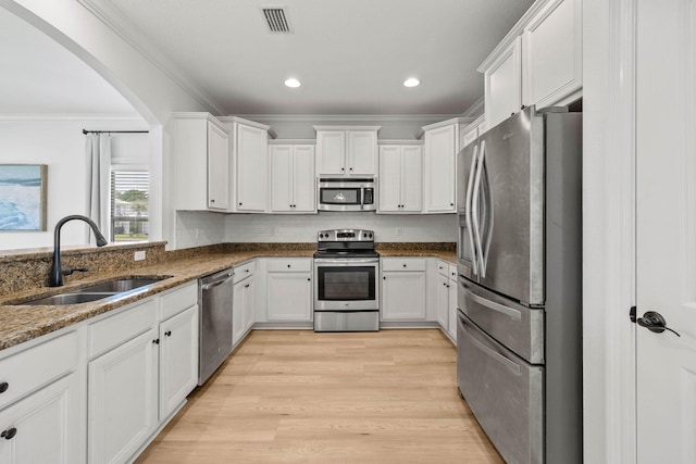 258 Tropical Breeze Dr, Santa Rosa Beach, FL 32459 - kitchen with appliances with stainless steel finishes, white cabinets, crown molding, dark stone countertops, and light wood-style floors