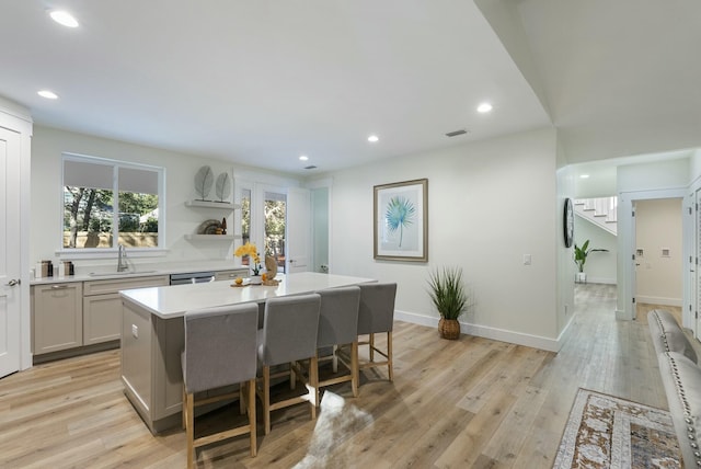 kitchen featuring a breakfast bar, a kitchen island, light wood-type flooring, gray cabinetry, and sink