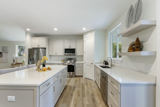 kitchen with appliances with stainless steel finishes, light wood-type flooring, a kitchen island, sink, and white cabinetry