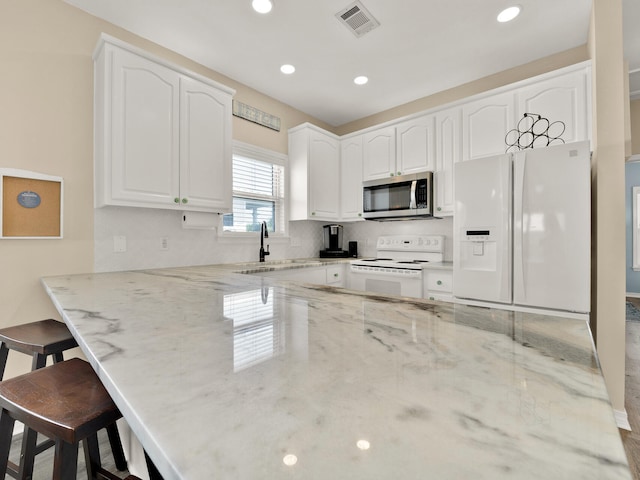 kitchen with sink, a kitchen breakfast bar, kitchen peninsula, white appliances, and white cabinets