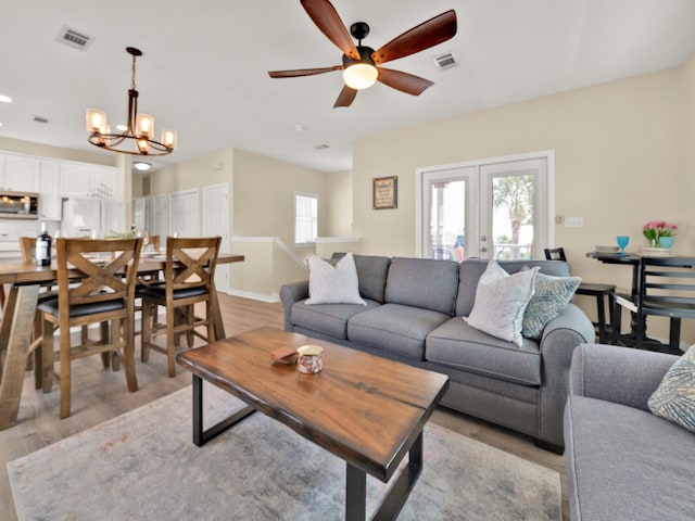 living room with ceiling fan with notable chandelier, light wood-type flooring, and french doors