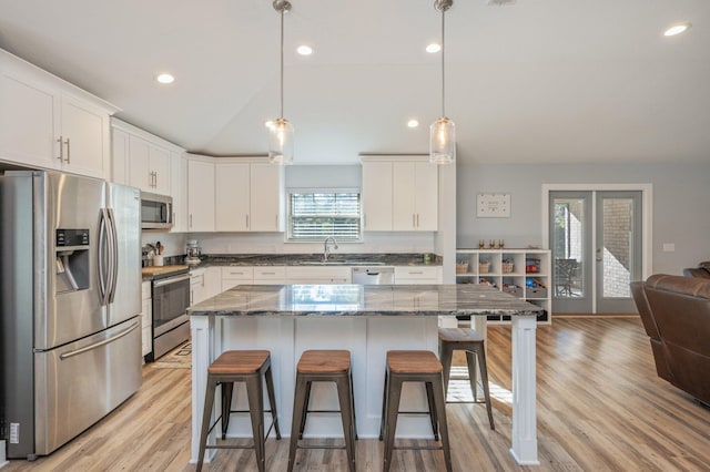 kitchen with stainless steel appliances, a kitchen island, dark stone countertops, pendant lighting, and white cabinets