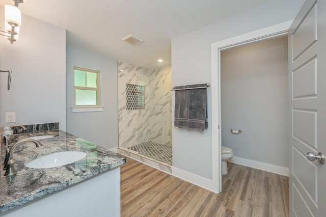 bathroom featuring toilet, vanity, hardwood / wood-style floors, and tiled shower