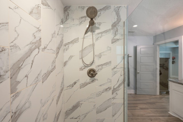 bathroom featuring hardwood / wood-style flooring, vanity, a textured ceiling, and tiled shower