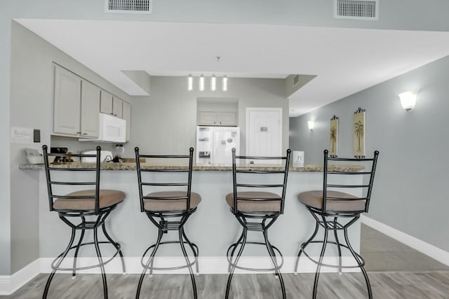 kitchen with kitchen peninsula, white appliances, light stone counters, and a breakfast bar area