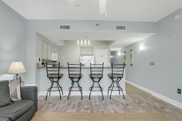 kitchen featuring white cabinetry, kitchen peninsula, white appliances, a breakfast bar, and light wood-type flooring